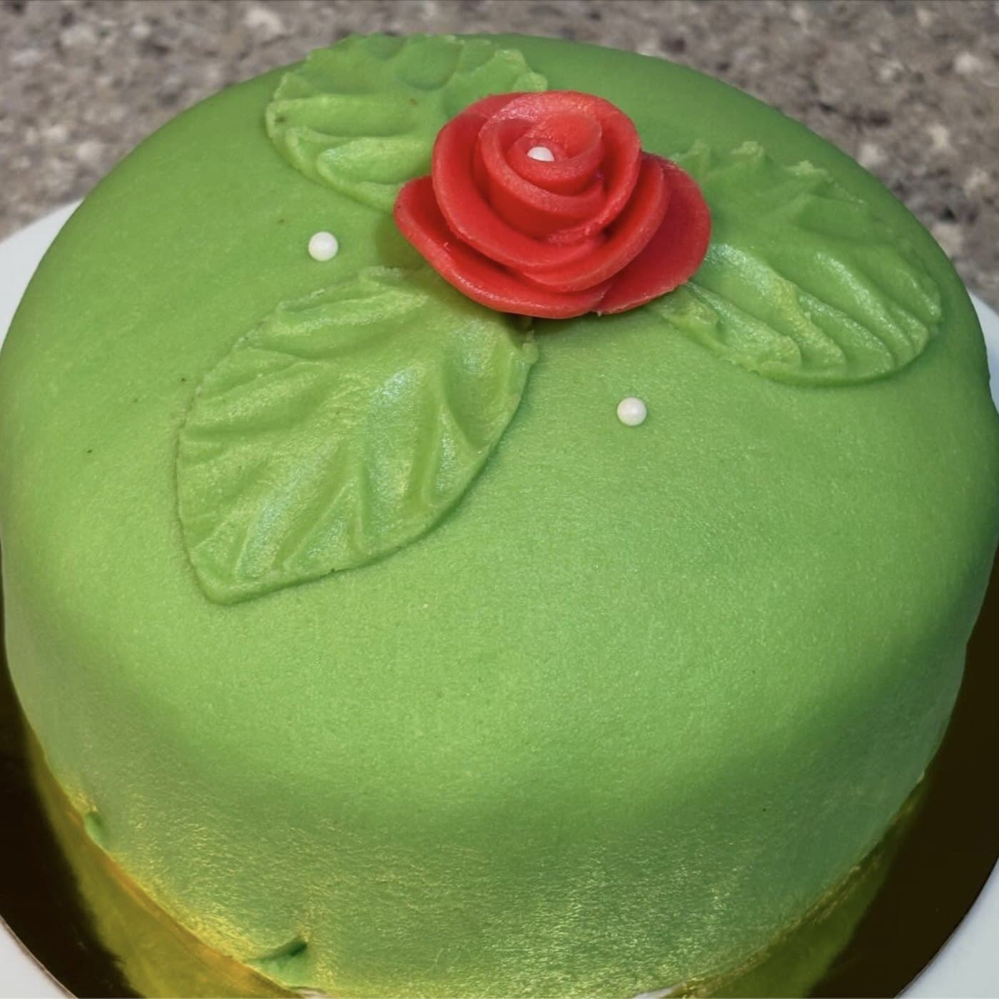 A traditional Swedish prinsesstårta covered in green marzipan with a red marzipan rose